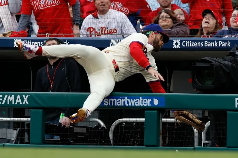 Phillies first baseman Bryce Harper falls into the television camera well attempting to catch a pop foul off the bat of the Braves' Austin Riley on Saturday.